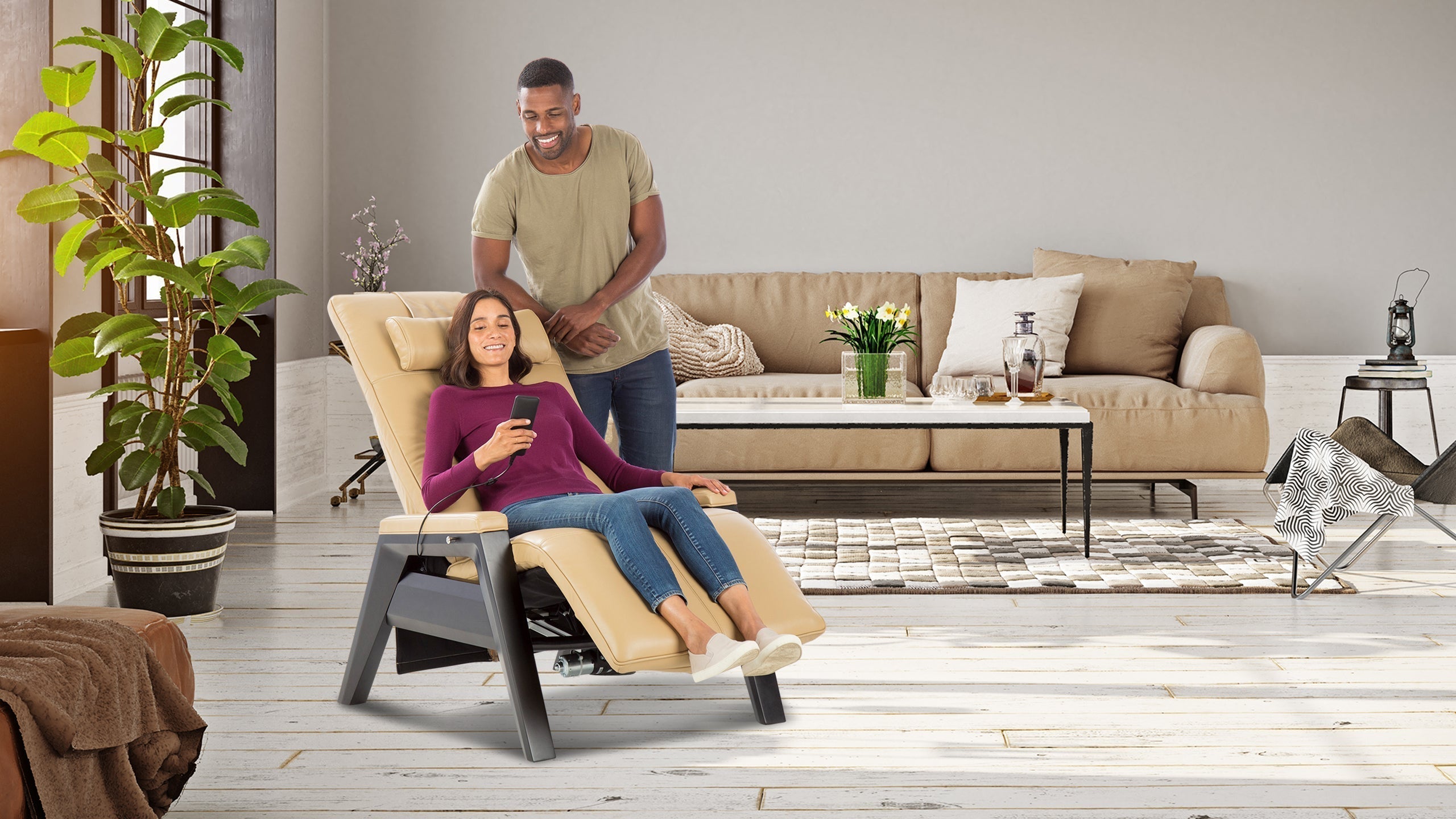 Woman relaxing in beige leather zero gravity recliner with remote while man stands beside her