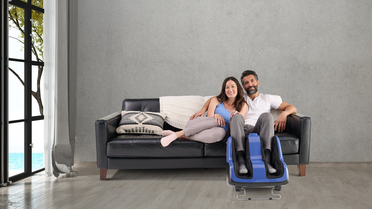 Couple relaxing on black leather sofa with man using blue foot and leg massager machine at home