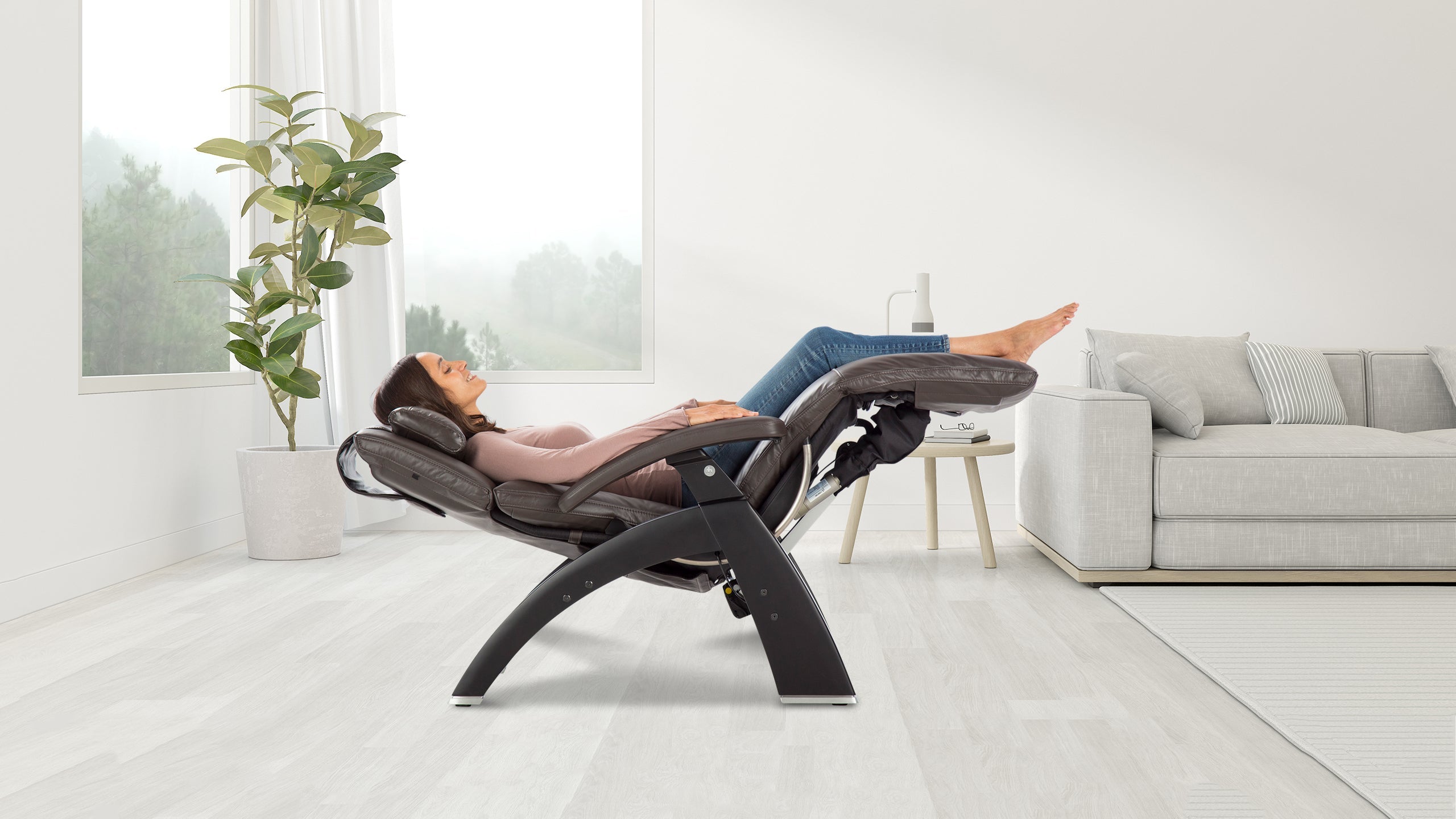 Woman reclining in a black zero-gravity massage chair with legs elevated in a bright living room
