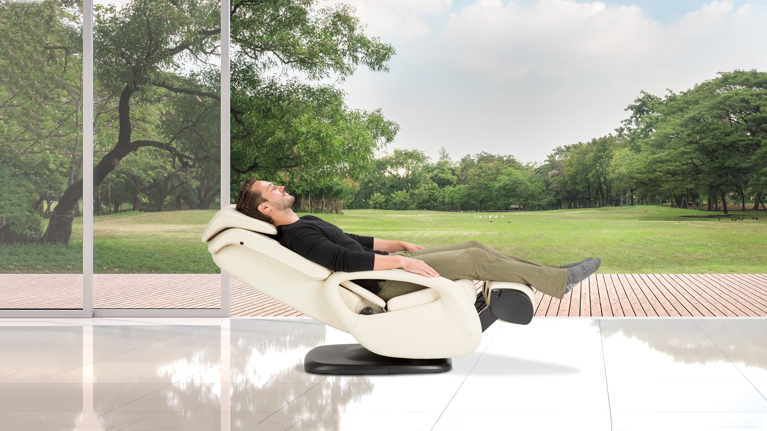 Man reclining with legs elevated in a cream massage chair in a glass-walled room overlooking a green park