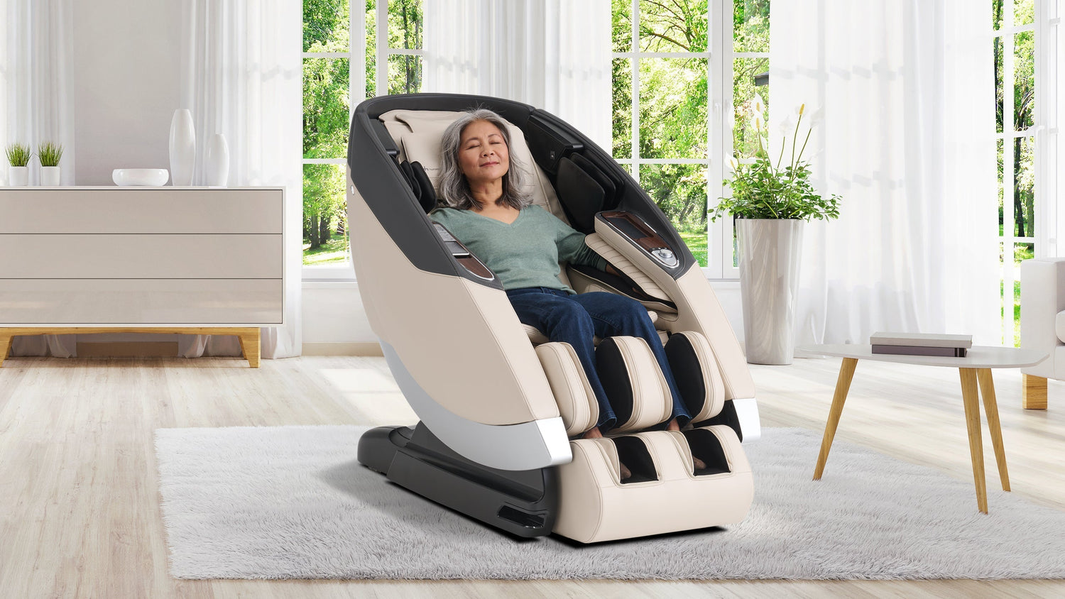 Older woman with gray hair relaxing in a beige and black full-body massage chair in a bright living room with large windows