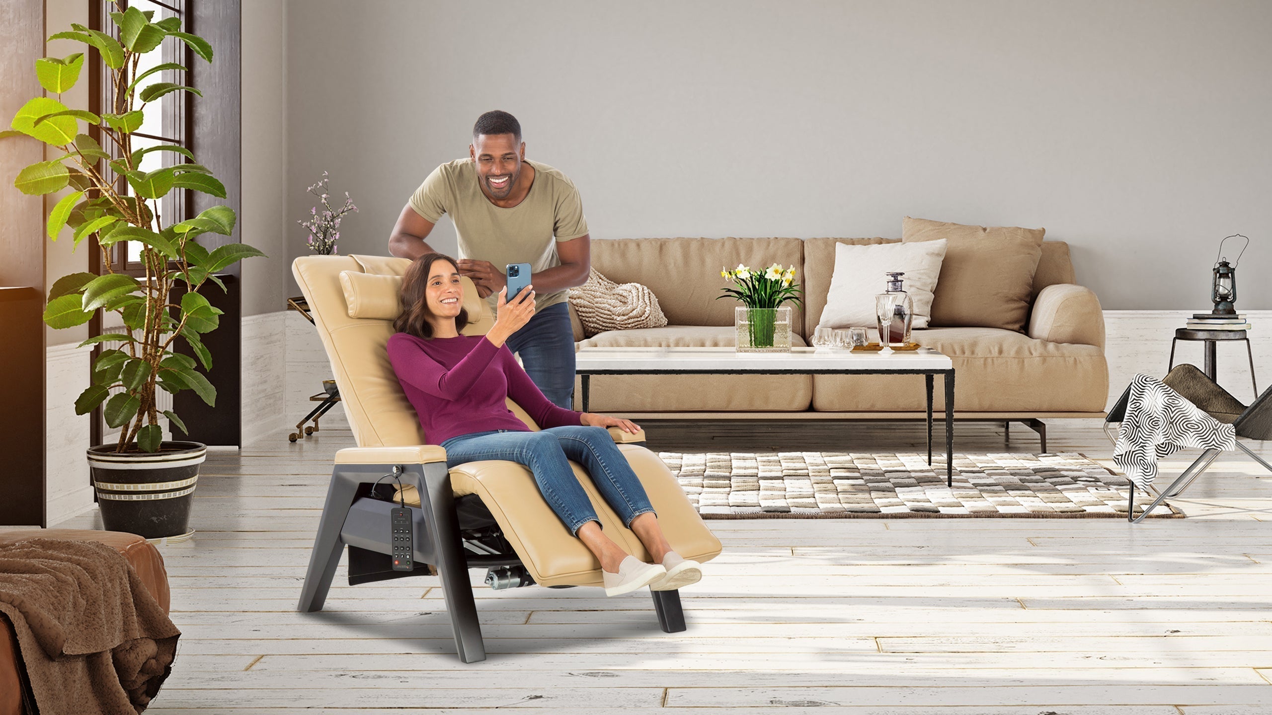 Woman sitting in beige leather zero gravity recliner chair with gray frame while man stands beside her in modern living room