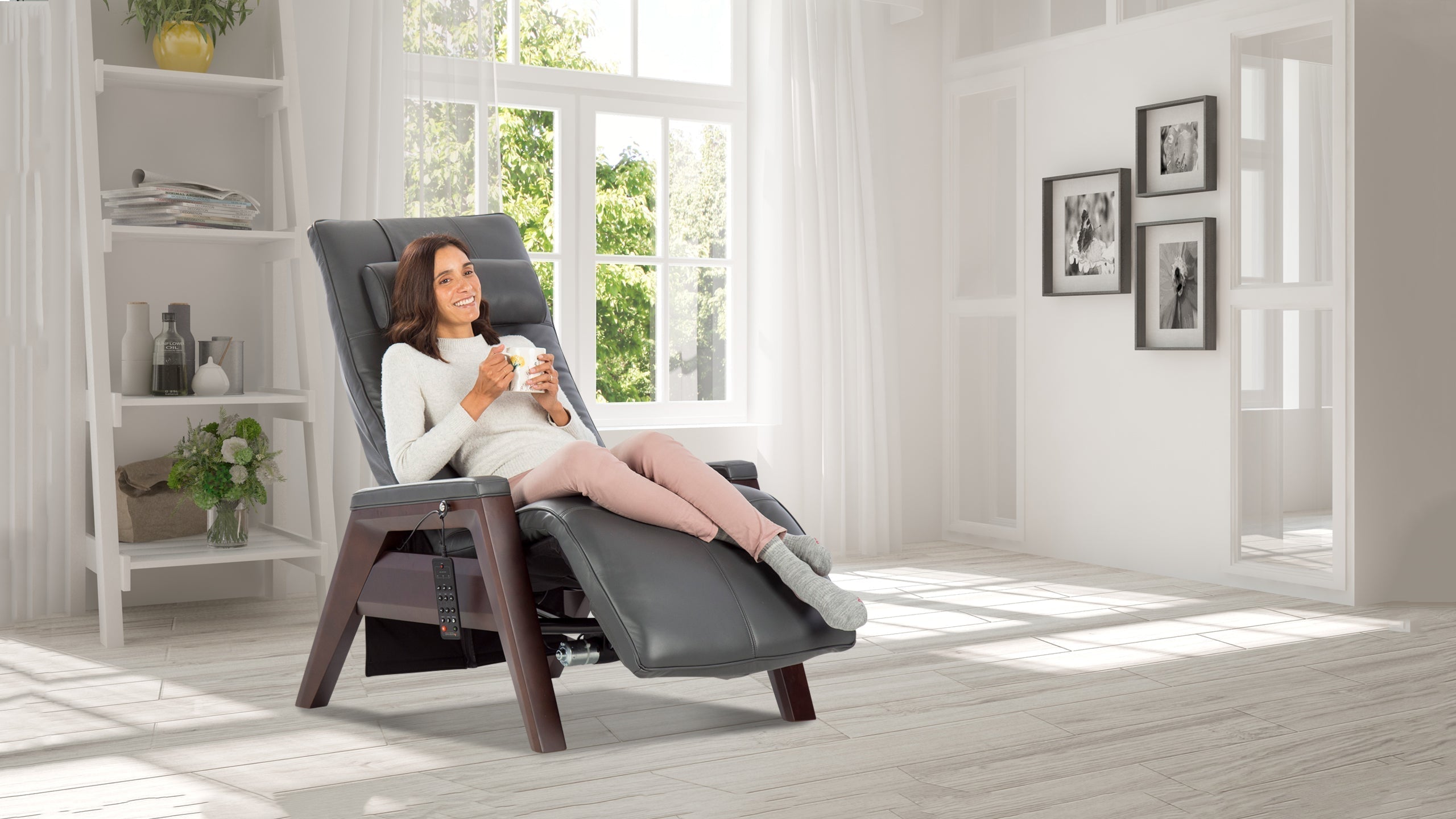 Smiling woman drinking coffee in a slate gray leather zero gravity recliner chair with dark walnut wood legs in a bright airy white living room