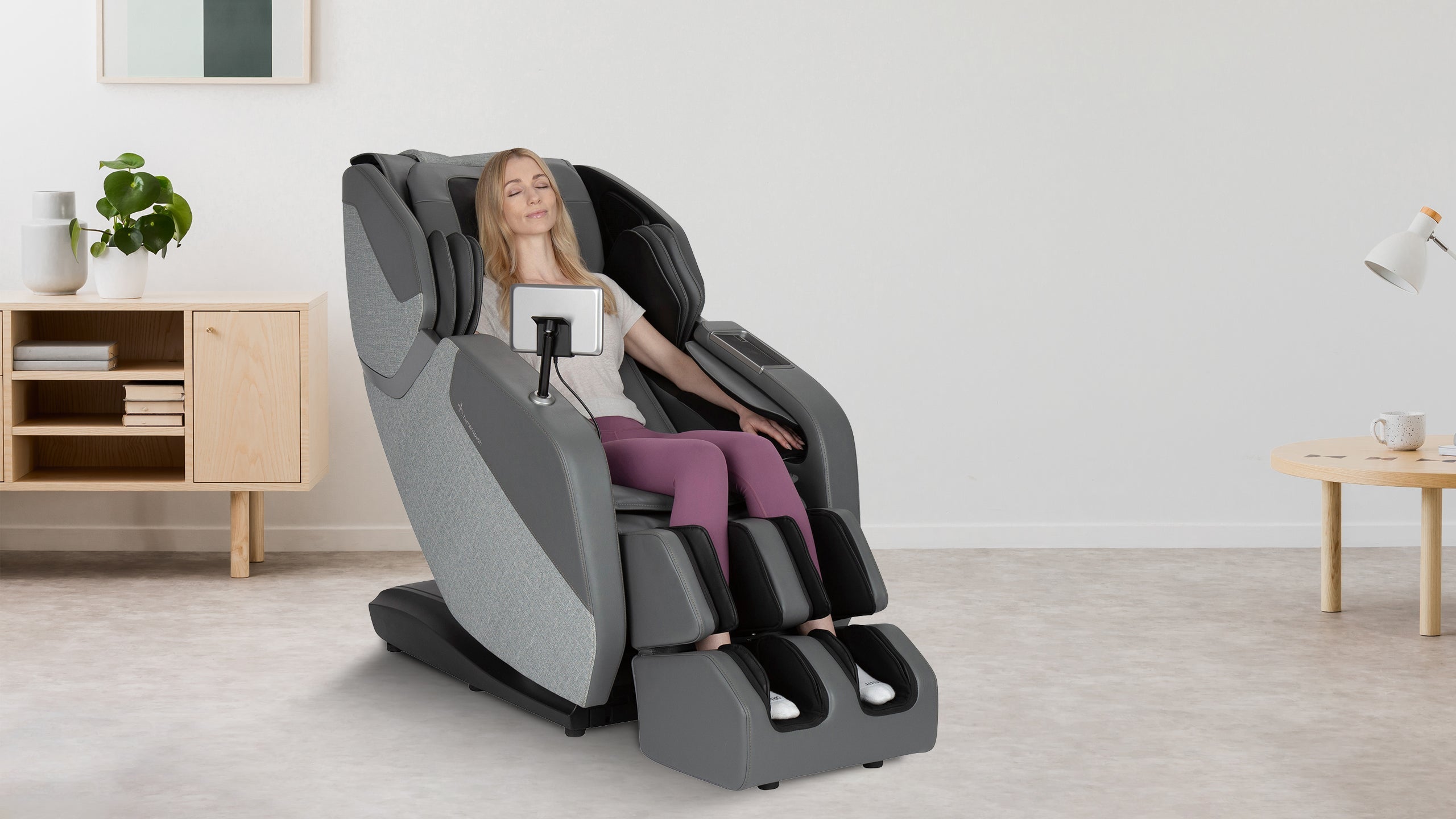 Woman relaxing in gray full body massage chair with tablet holder and calf foot rollers