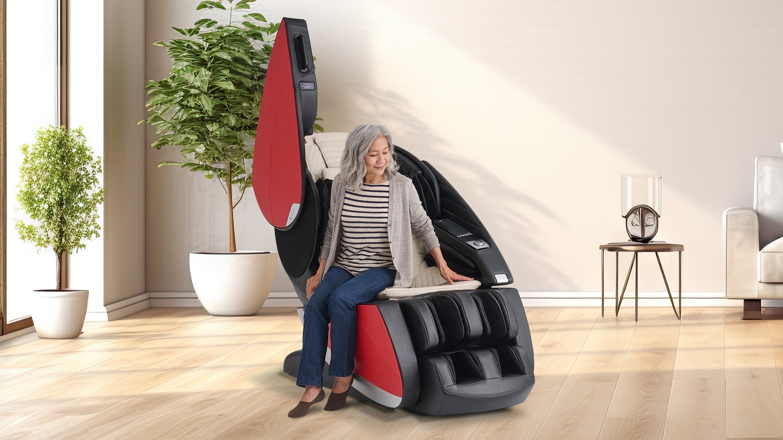 Older woman with gray hair sitting in a black and red massage chair with open side panel in a bright living room