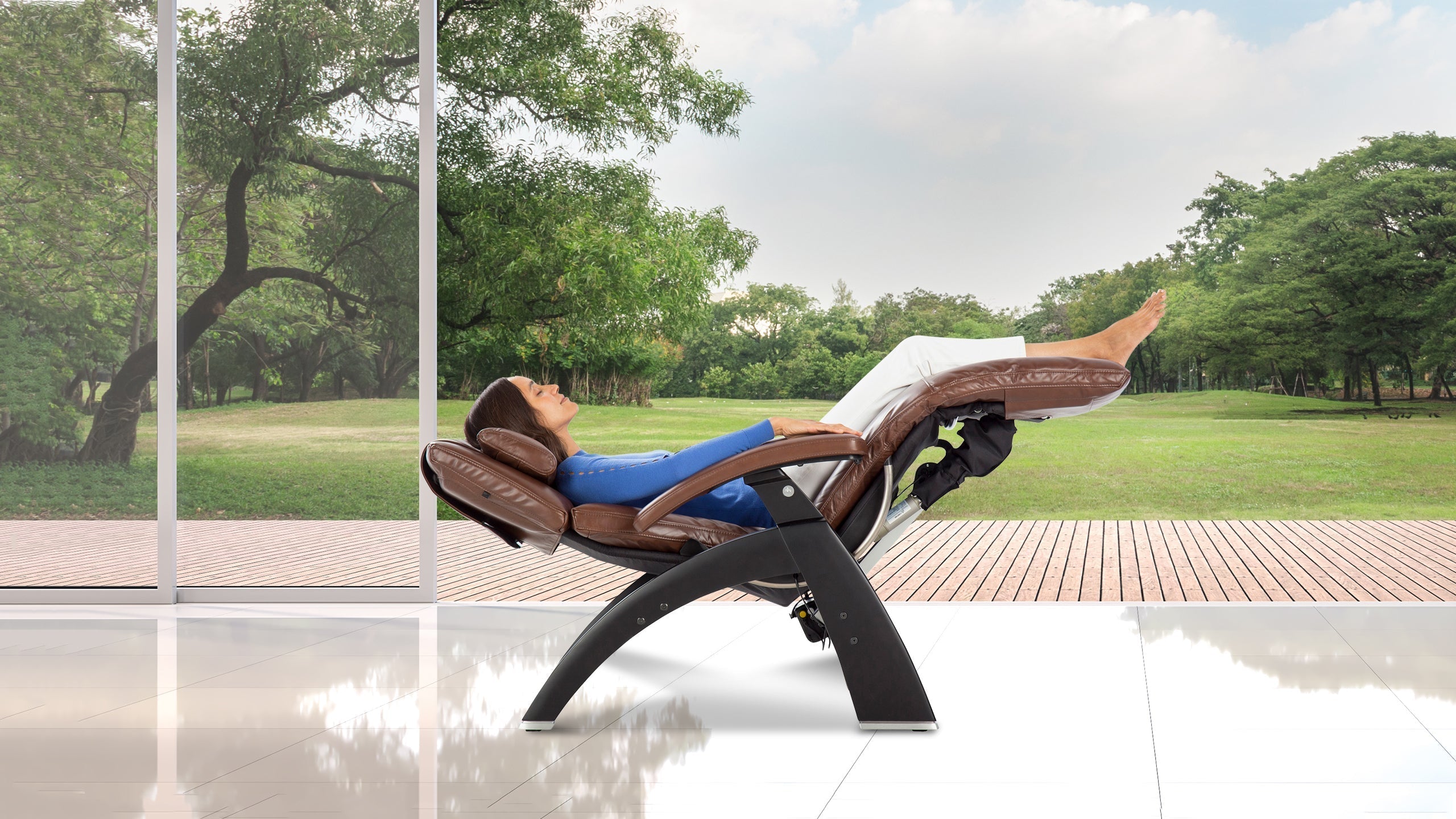 Woman reclining with legs elevated in a tan leather zero gravity chair with black frame overlooking a park
