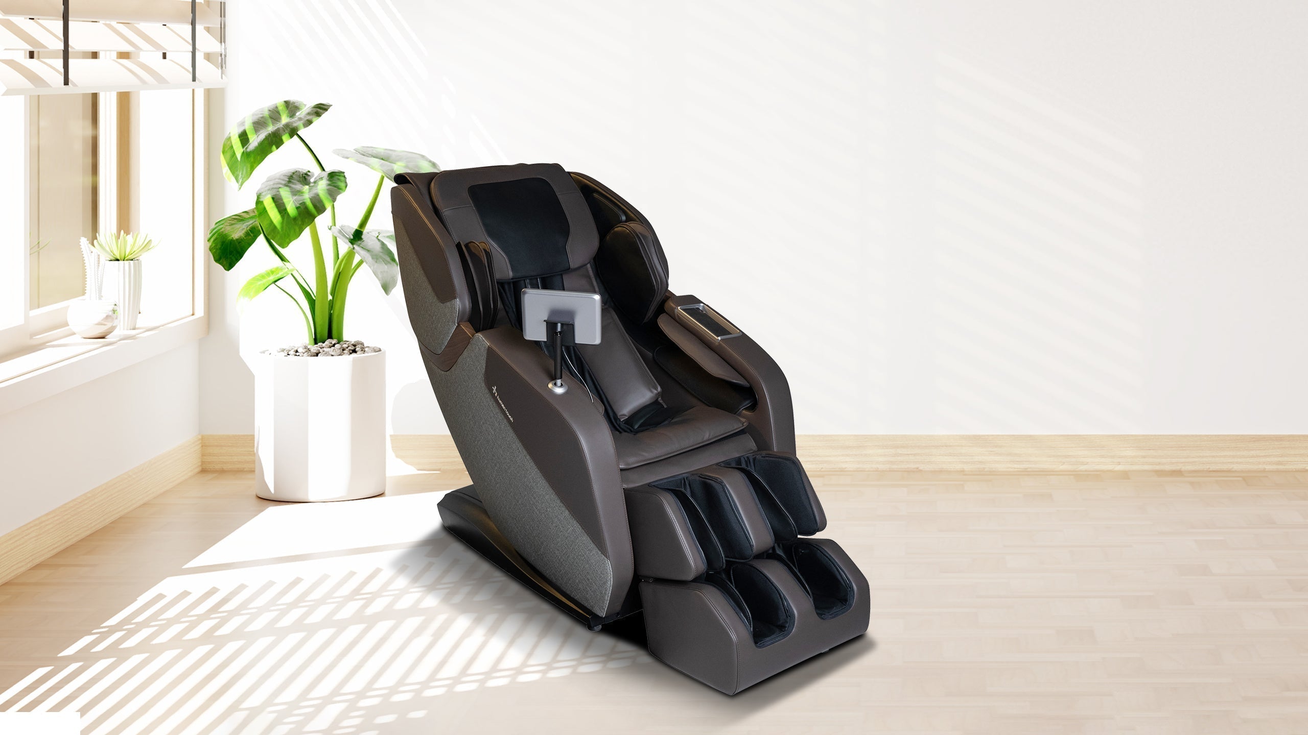 Dark brown full-body massage chair with tablet arm in a bright minimalist room with an indoor plant