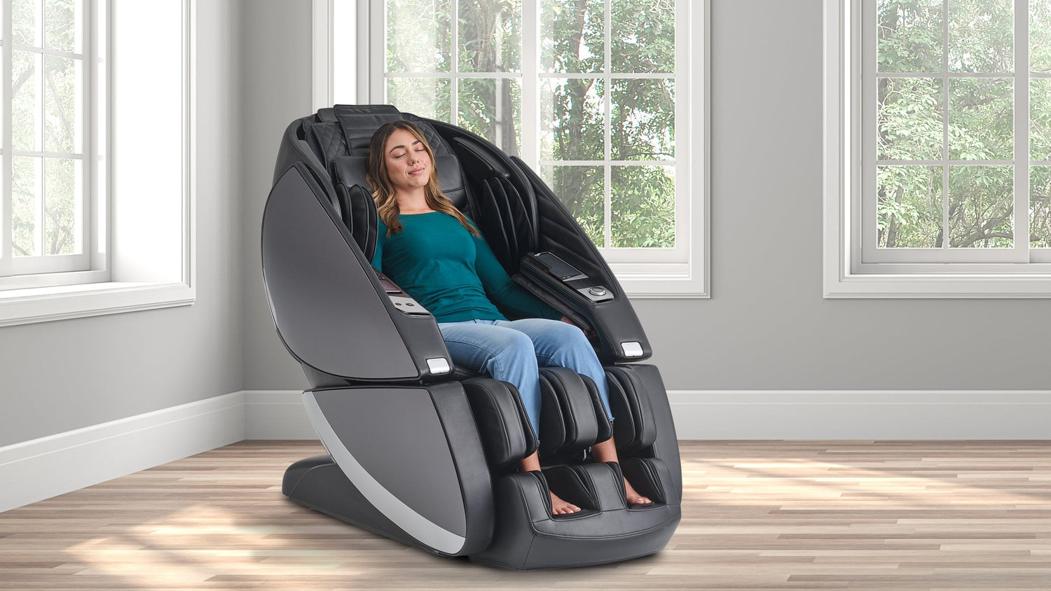Woman relaxing with eyes closed in a black full-body massage chair in a bright room with large windows and trees outside