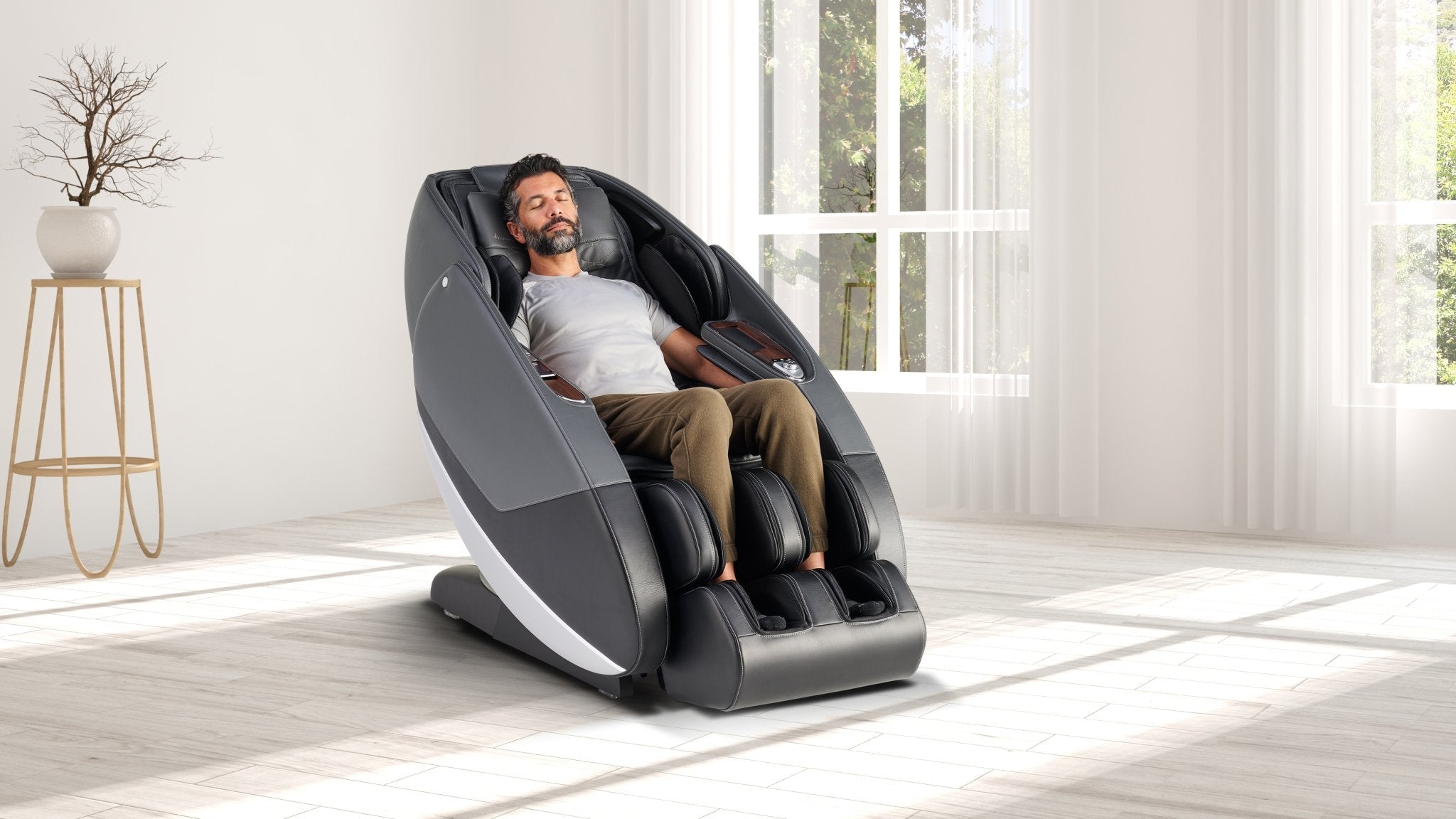 Man relaxing with eyes closed in gray full body massage chair in bright white living room