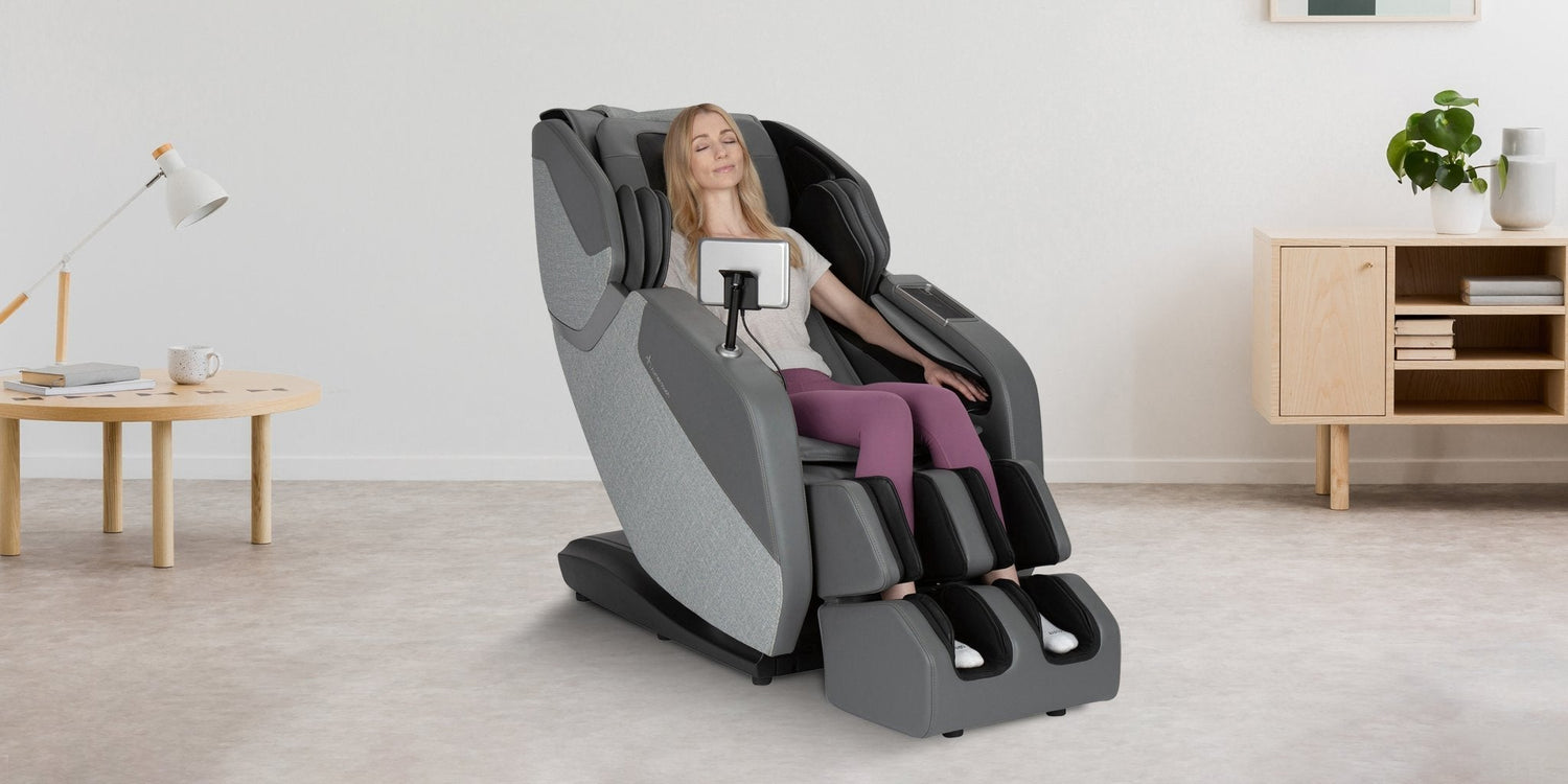Woman relaxing with eyes closed in gray full body massage chair with tablet holder in Scandinavian living room