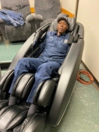 LA Firefighter using a massage chair in a room with gray carpet and furniture.