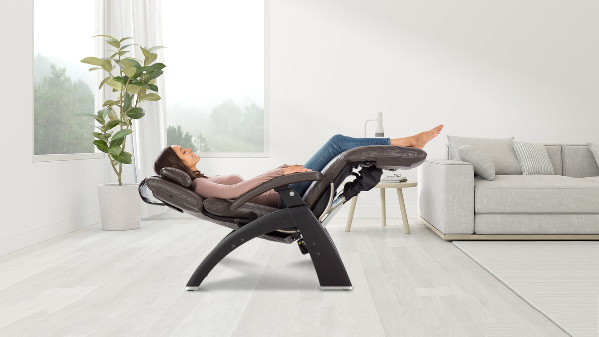 Woman reclining in a black zero-gravity massage chair with legs elevated in a bright living room