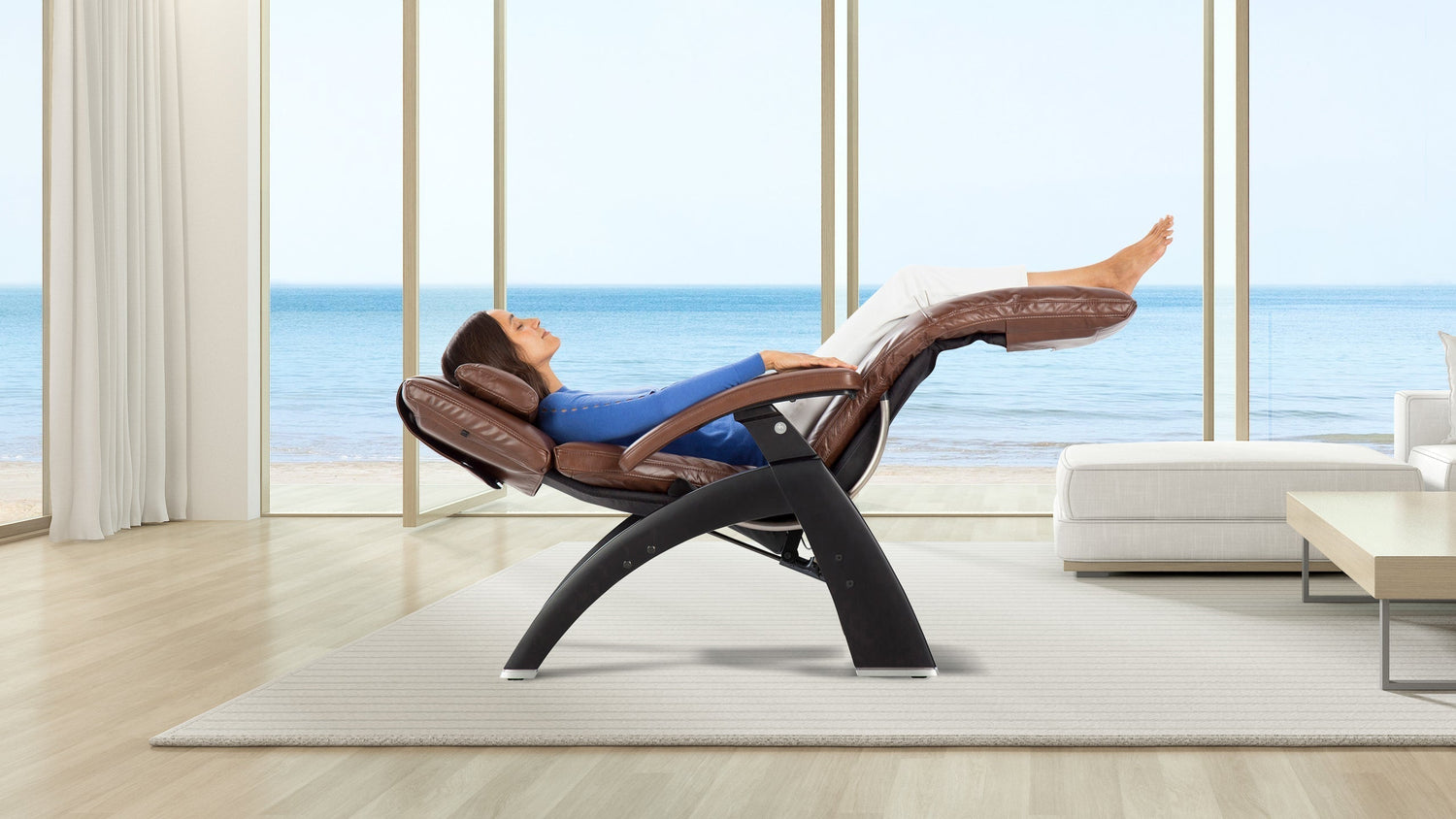 Woman reclining in zero gravity chair with brown leather cushions and black frame by ocean view window