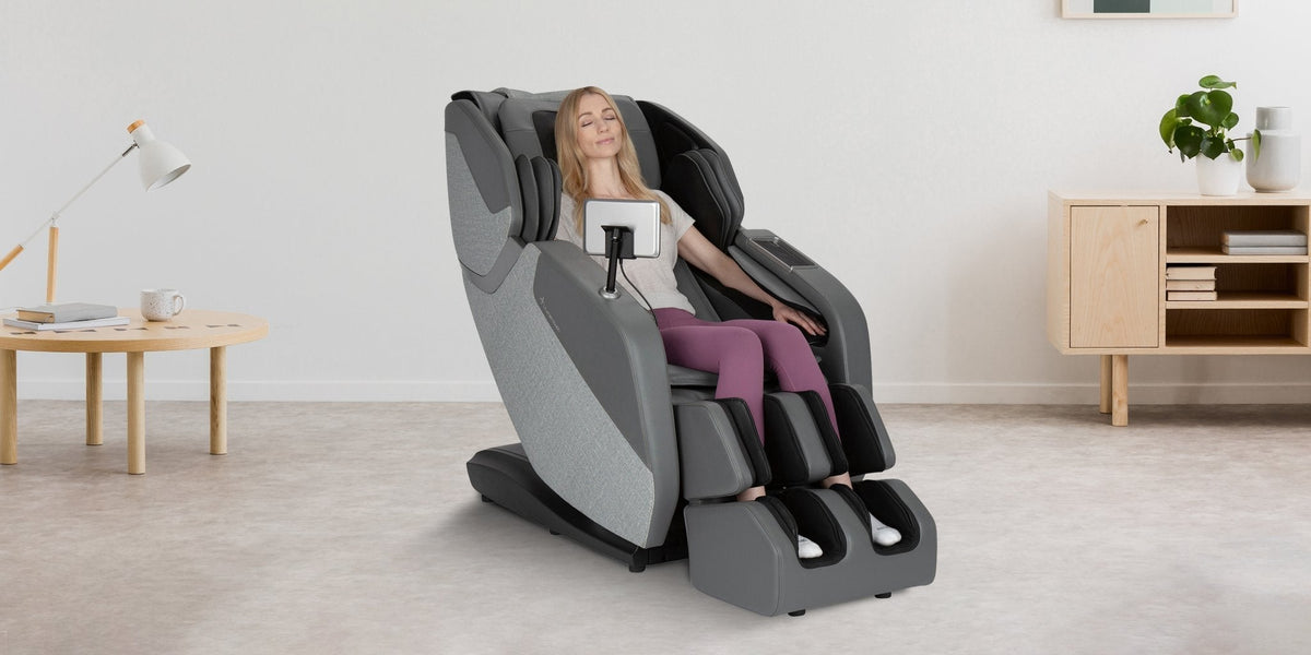 Woman relaxing with eyes closed in gray full body massage chair with tablet holder in Scandinavian living room