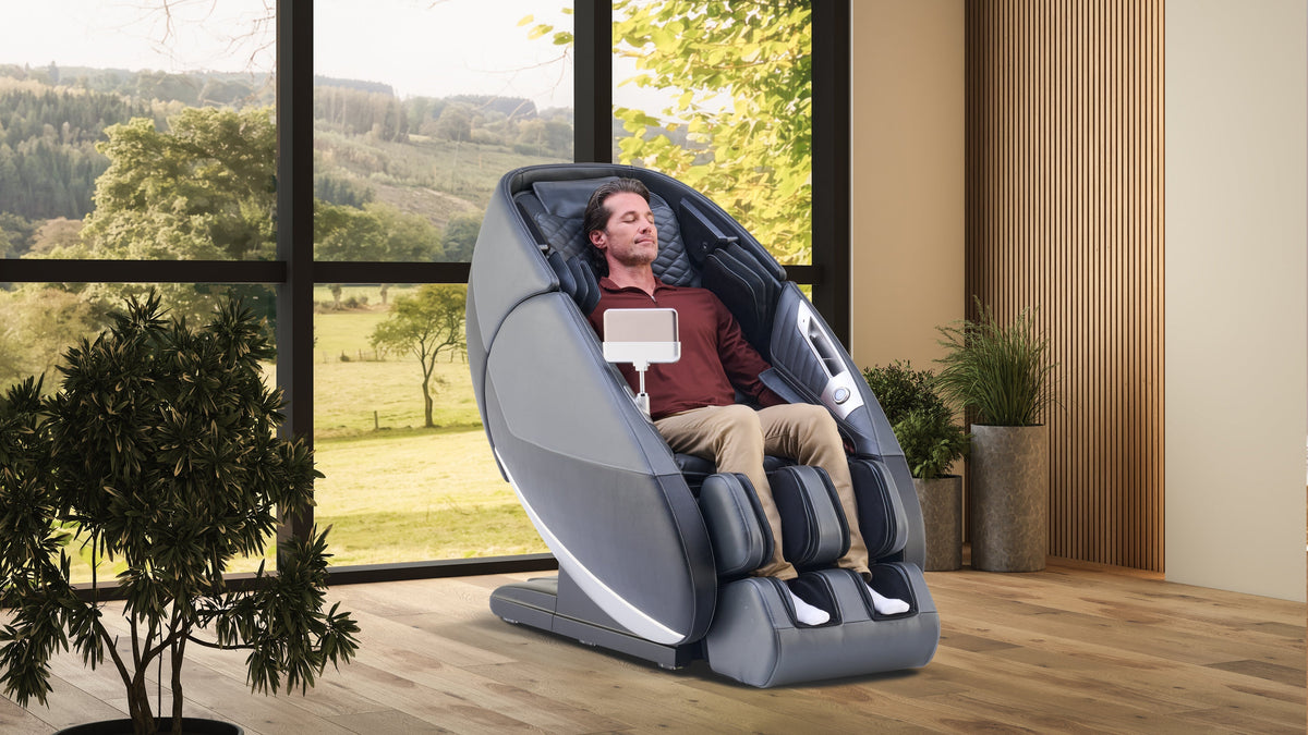 Man using a massage chair in a room with large windows and greenery outside