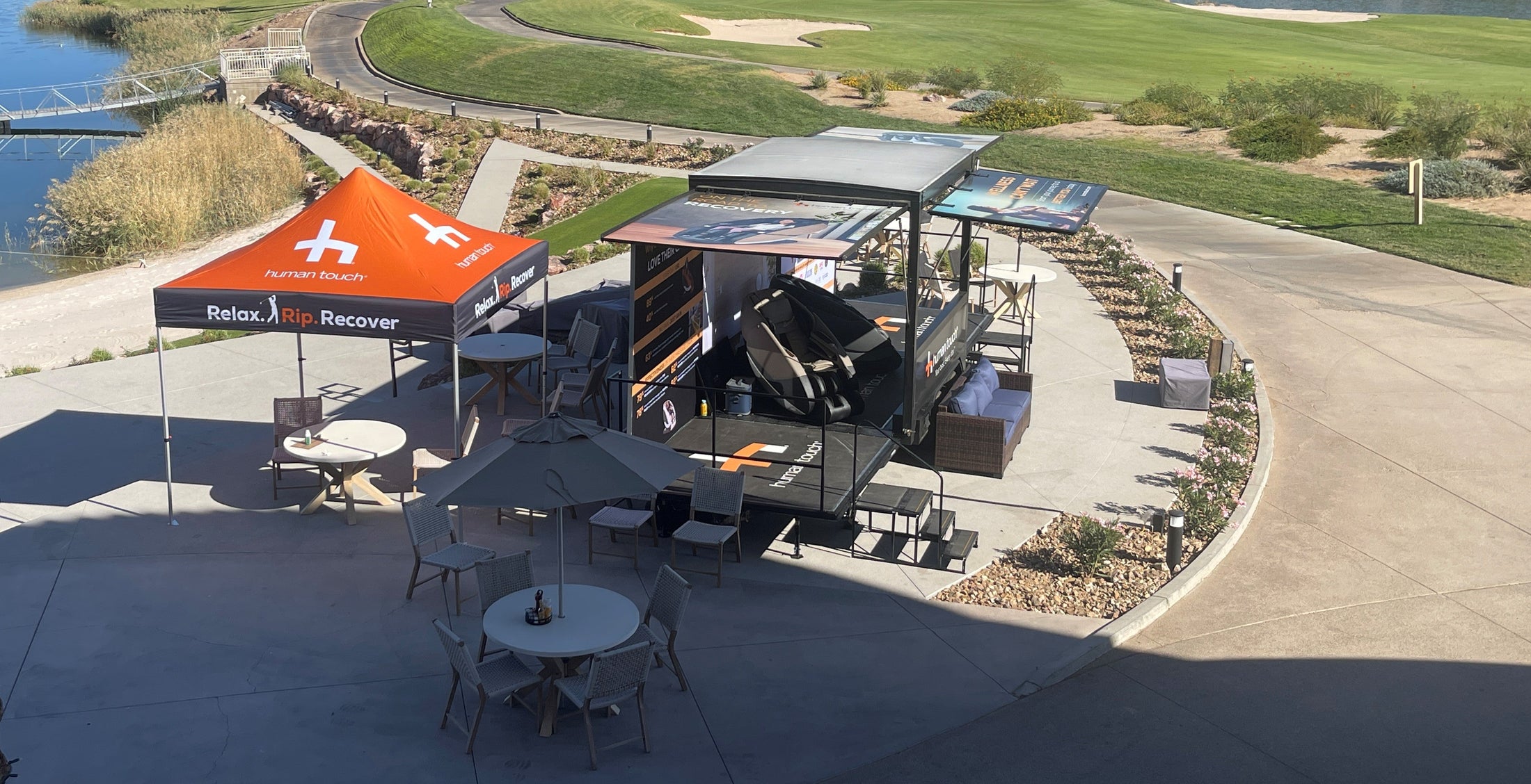 Outdoor patio area with tables, chairs, and a large umbrella near a golf course and lake.