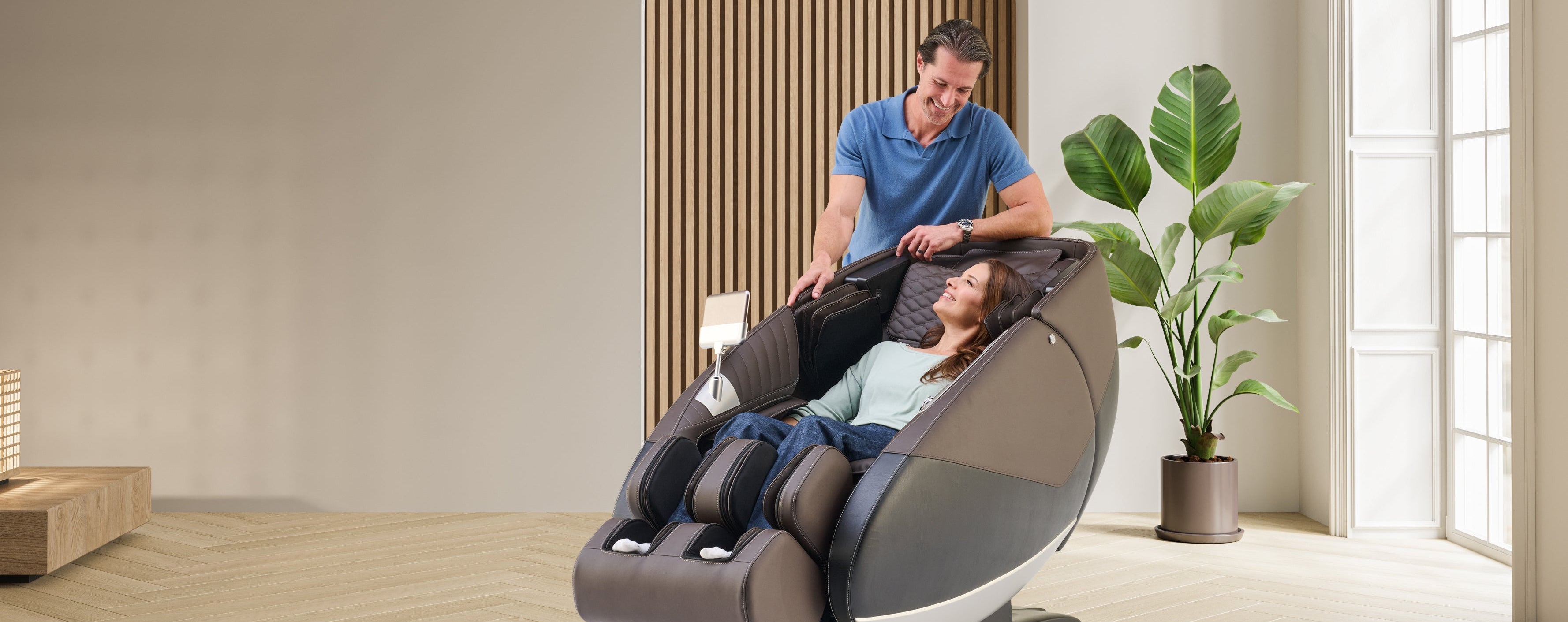 Man assisting a woman in a massage chair in a modern living room.