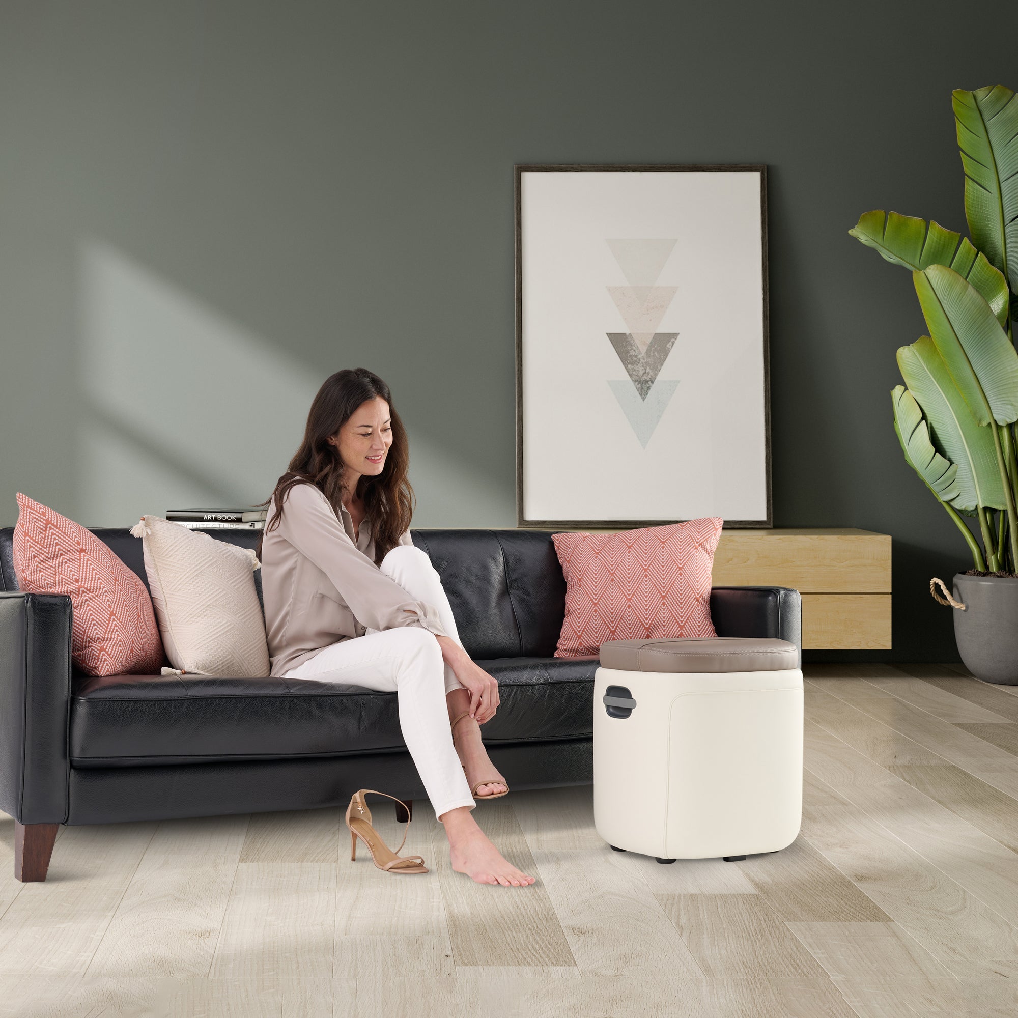 Reveal Ottoman Massager shown in modern living room with woman relaxing on couch using foot massage feature