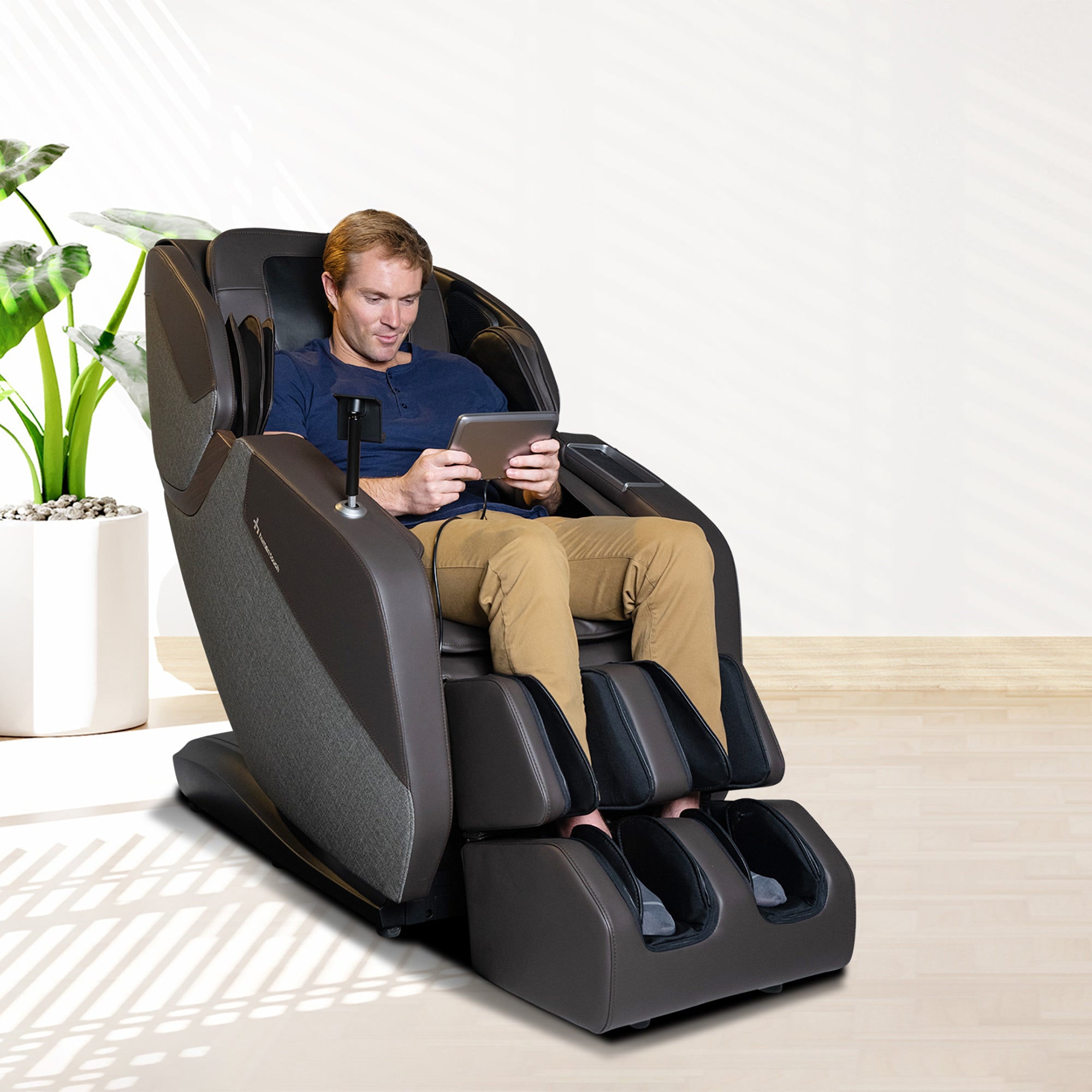 WholeBody ROVE massage chair shown in modern setting with person relaxing while using tablet in luxurious black chair